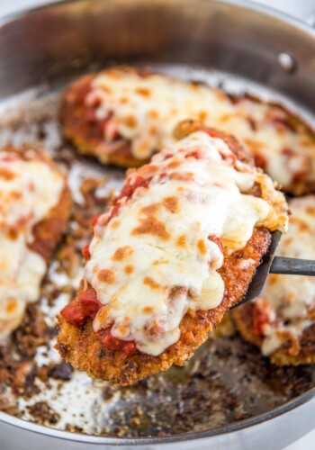 Chicken parmesan being lifted out of a skillet with a spatula.