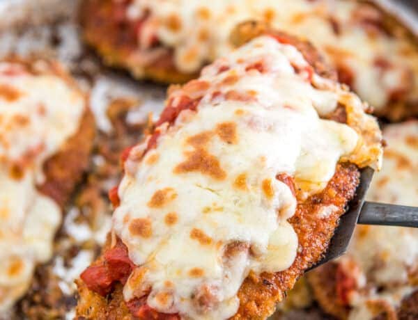 Chicken parmesan being lifted out of a skillet with a spatula.