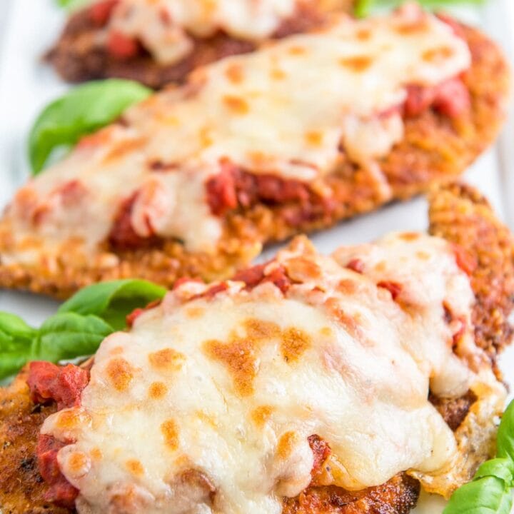 Three pieces of chicken parm on a serving plate with fresh basil garnish.