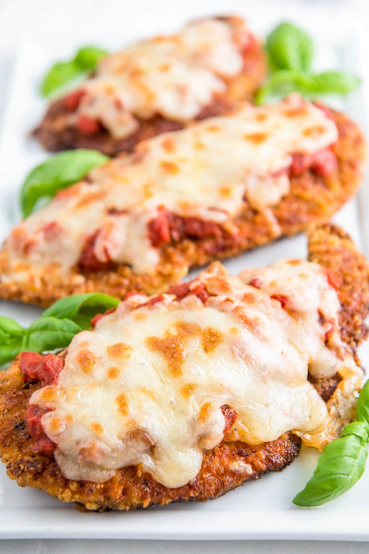 Three pieces of chicken parm on a serving plate with fresh basil garnish.