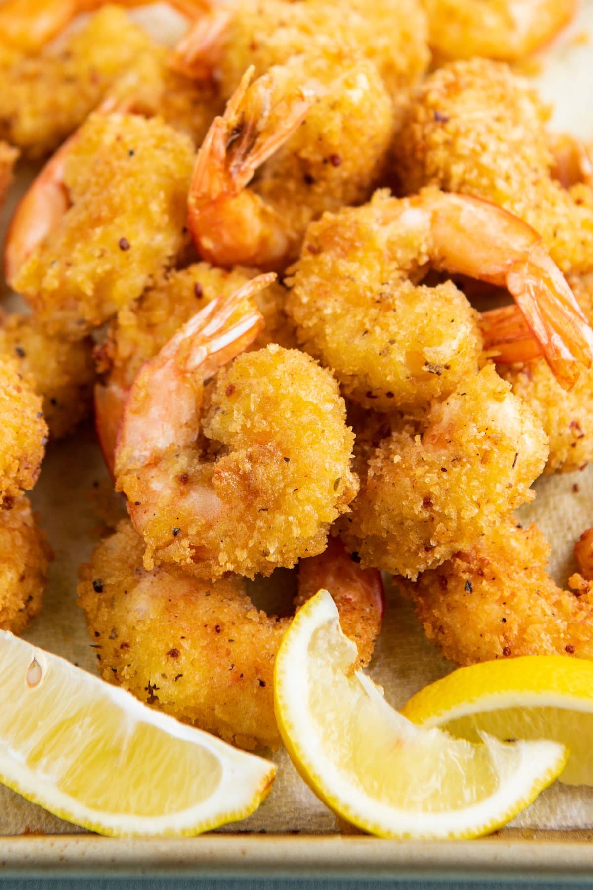 Fried shrimp on a cookie sheet with lemon wedges.