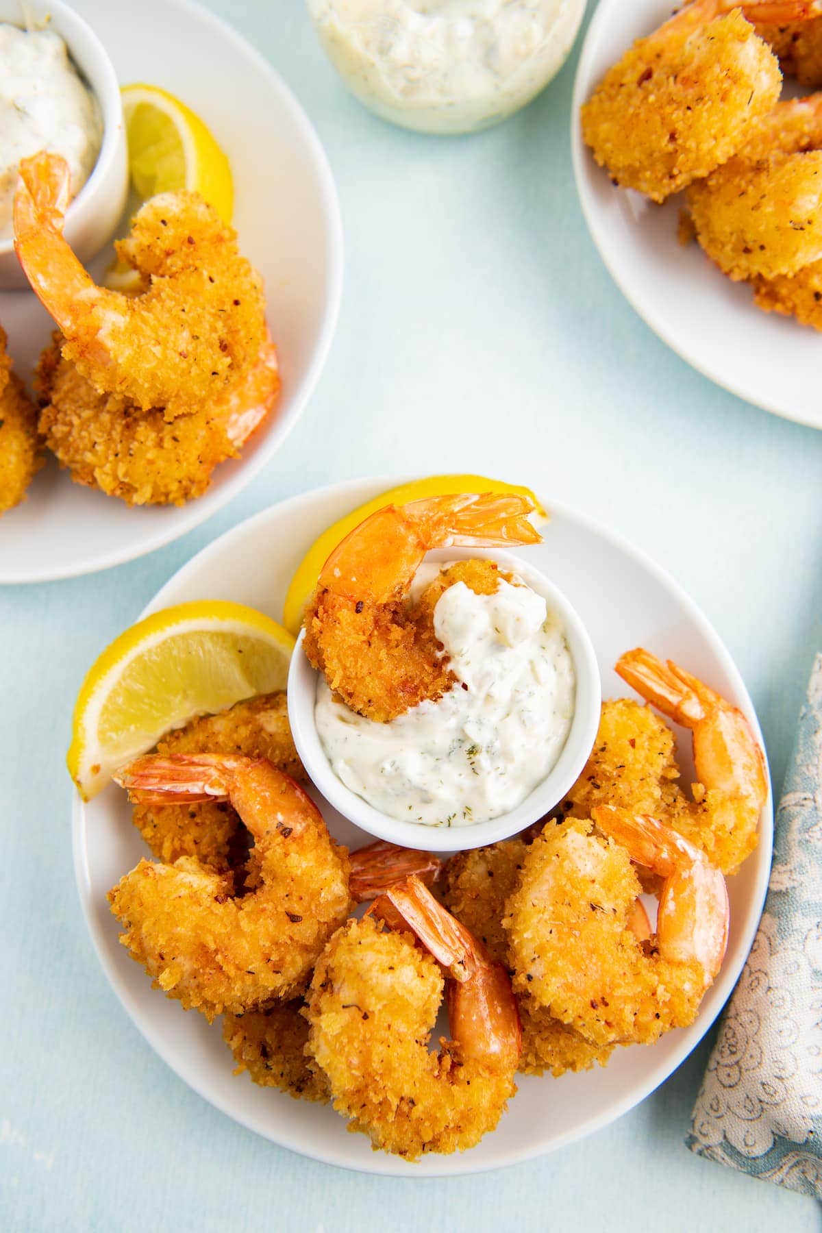 Crispy shrimp on white plates with a bowl of tartar sauce for dipping.