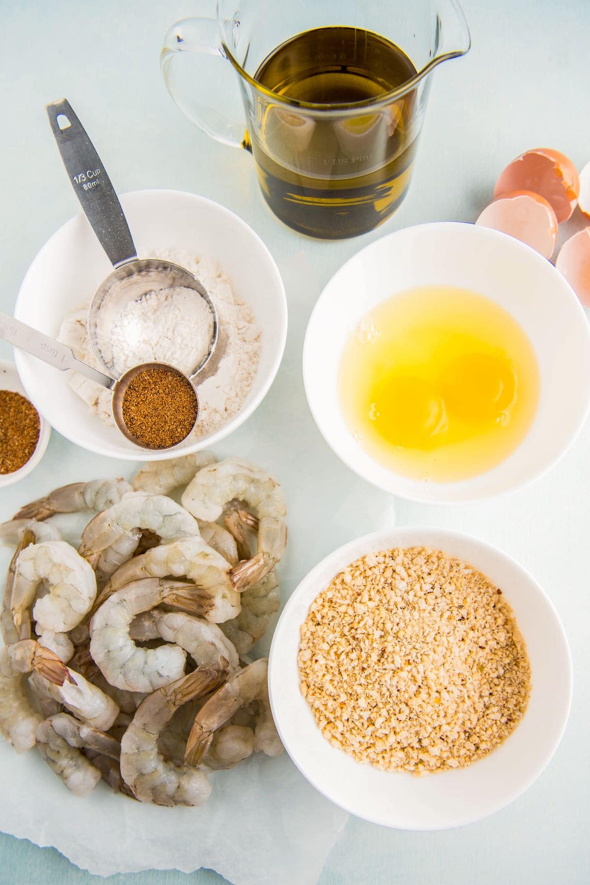 Ingredients in bowls and raw shrimp on parchment paper.