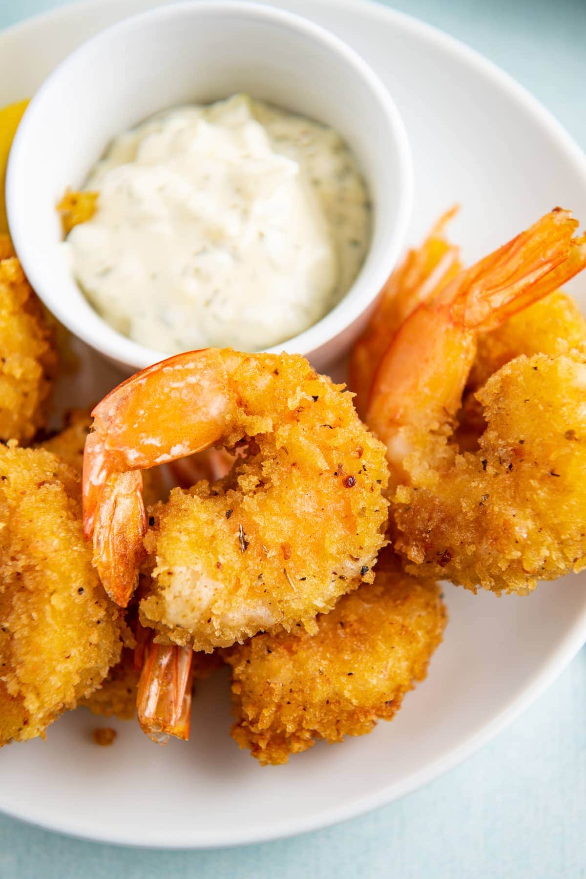 Fried shrimp on a white plate with a bowl of tartar sauce.