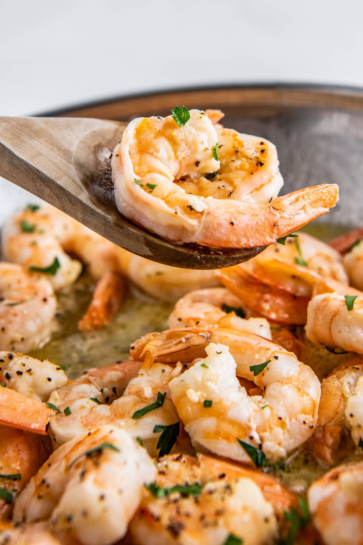 A wooden spoon scooping up shrimp out of a skillet.
