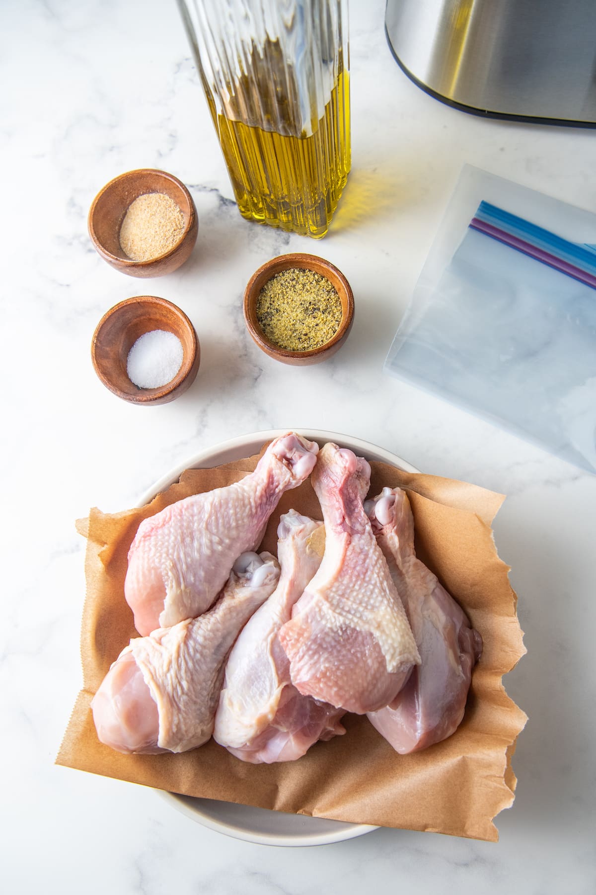 a bowl of uncooked chicken drumsticks alongside prep bowls with seasonings