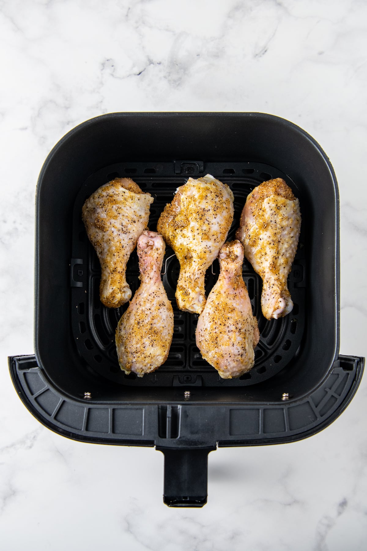 four seasoned lemon pepper chicken drumsticks in an air fryer basket