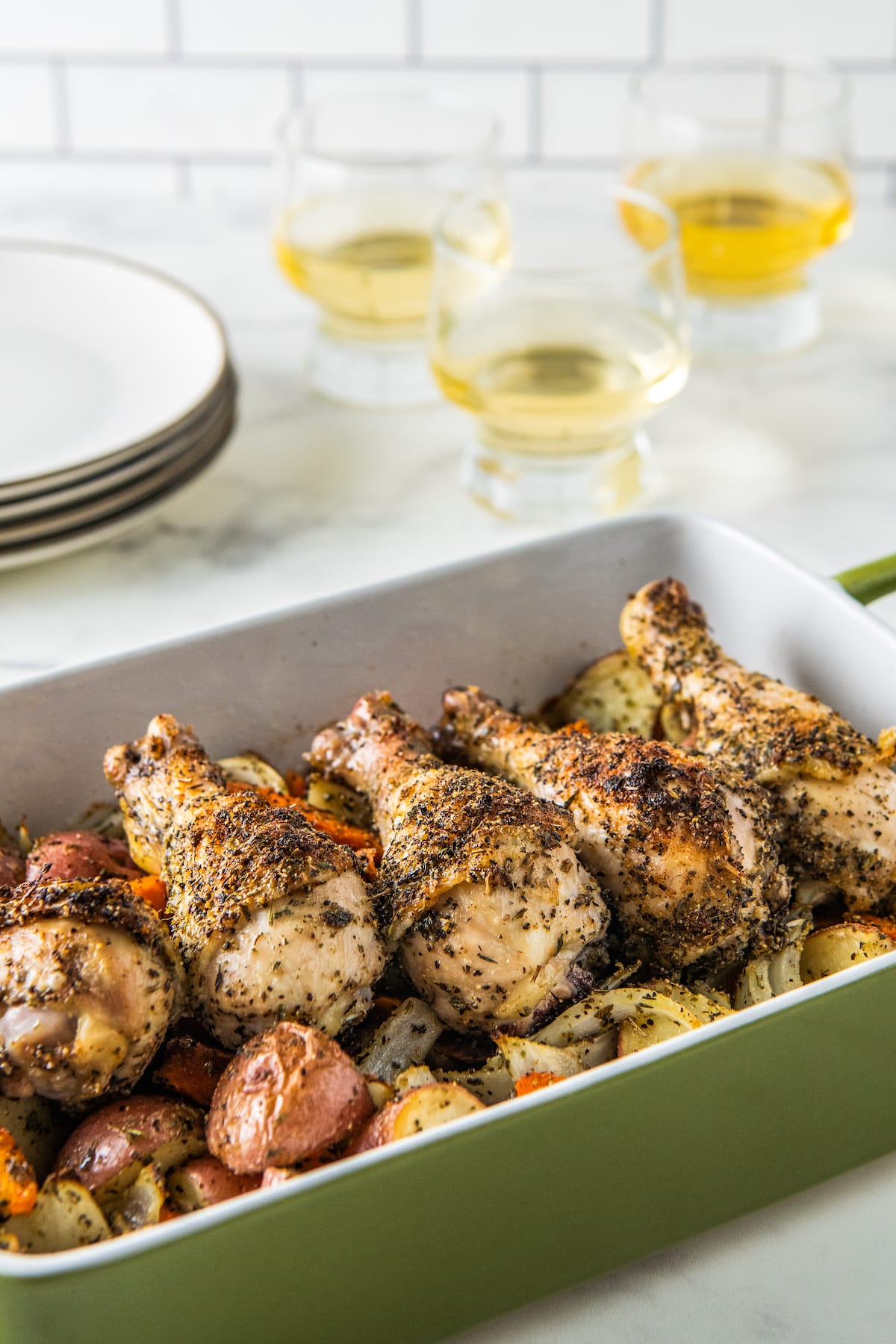 seasoned chicken legs in a baking dish on top of a vegetable assortment