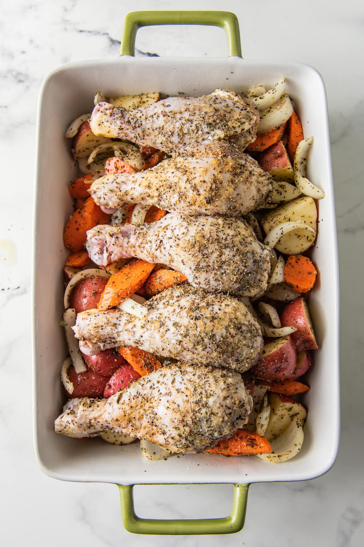 seasoned chicken legs in a baking dish on top of a vegetable assortment