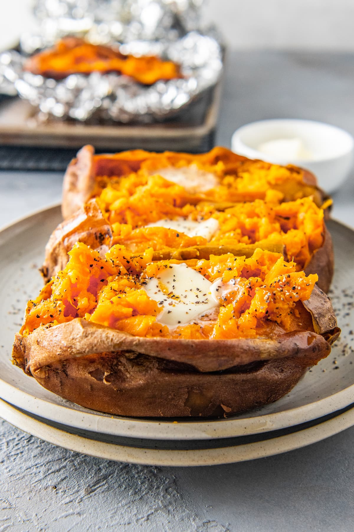 three baked sweet potatoes with butter, salt, and pepper on a plate