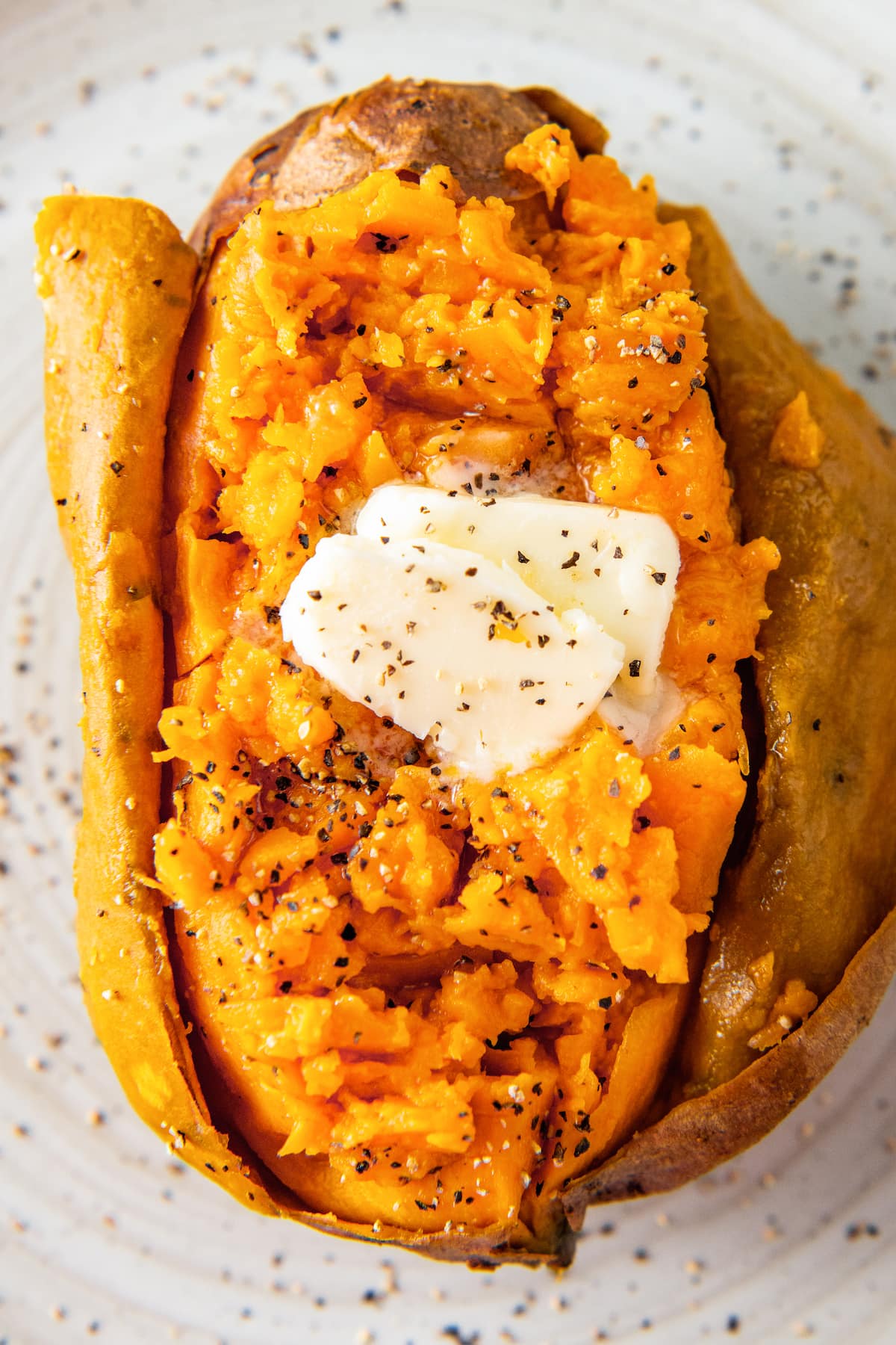 close up of a baked sweet potato with butter, salt, and pepper