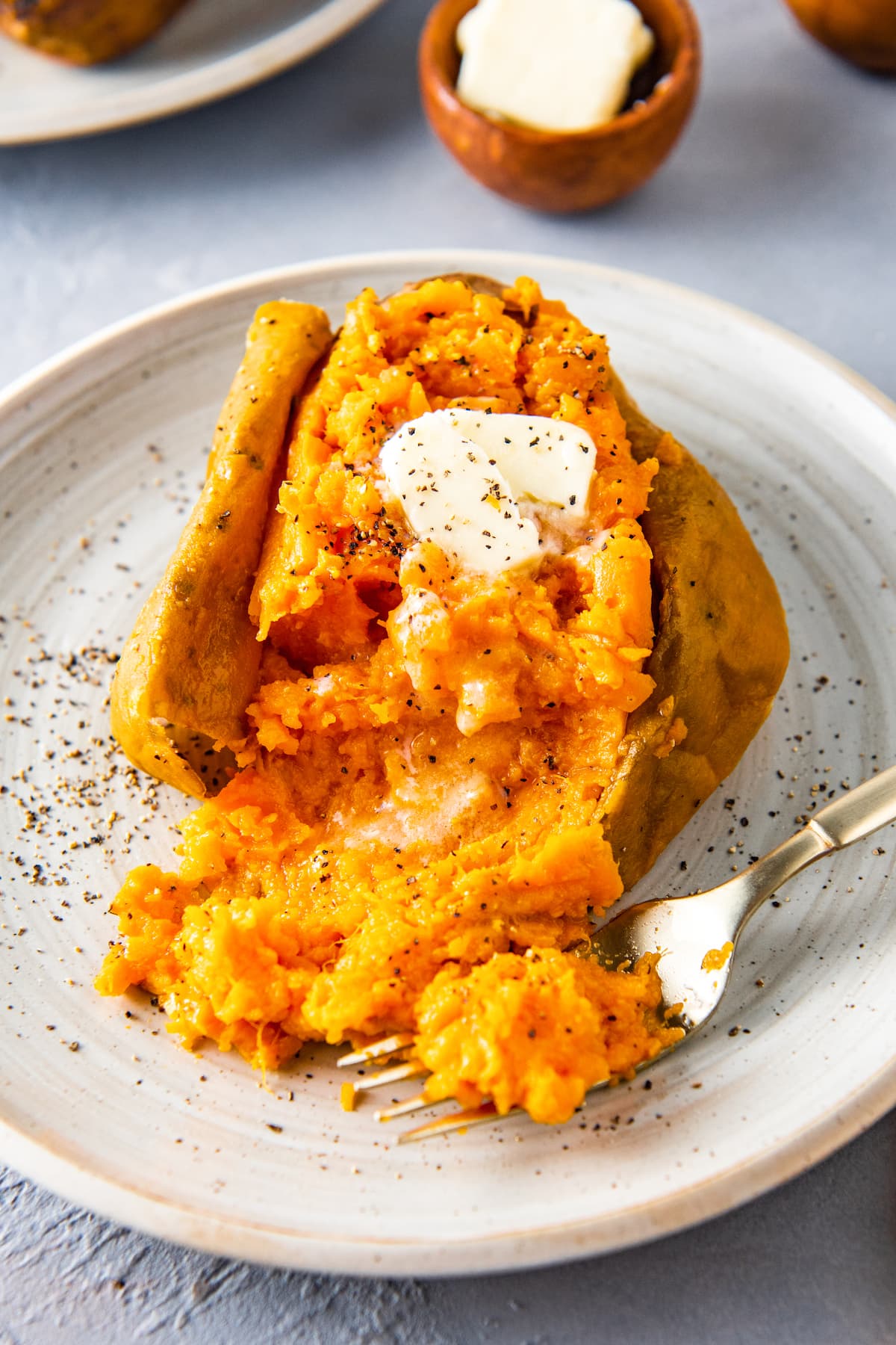 baked sweet potato with butter on a plate and a fork taking a bite out