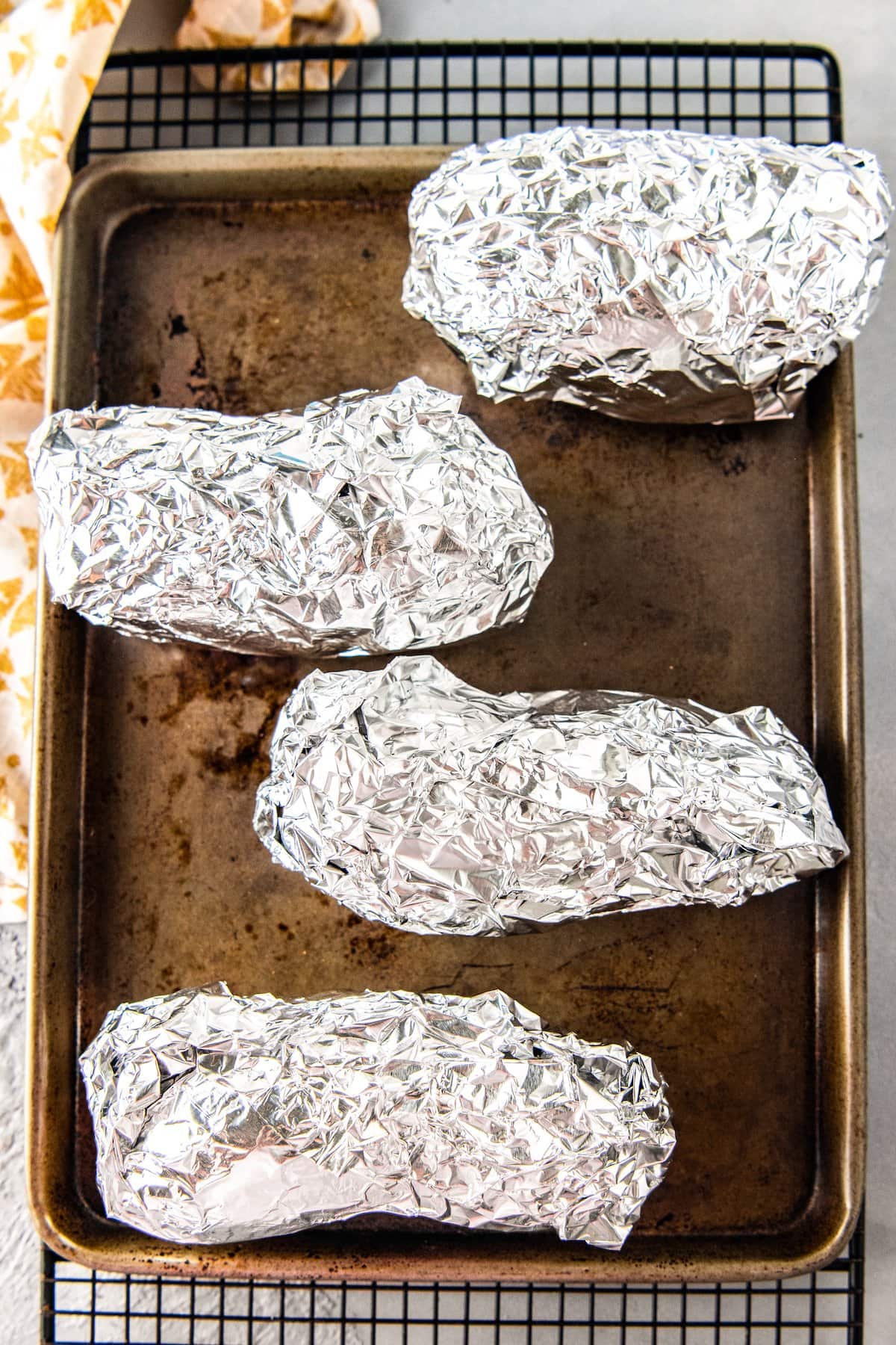four potatoes wrapped in foil on a cookie sheet