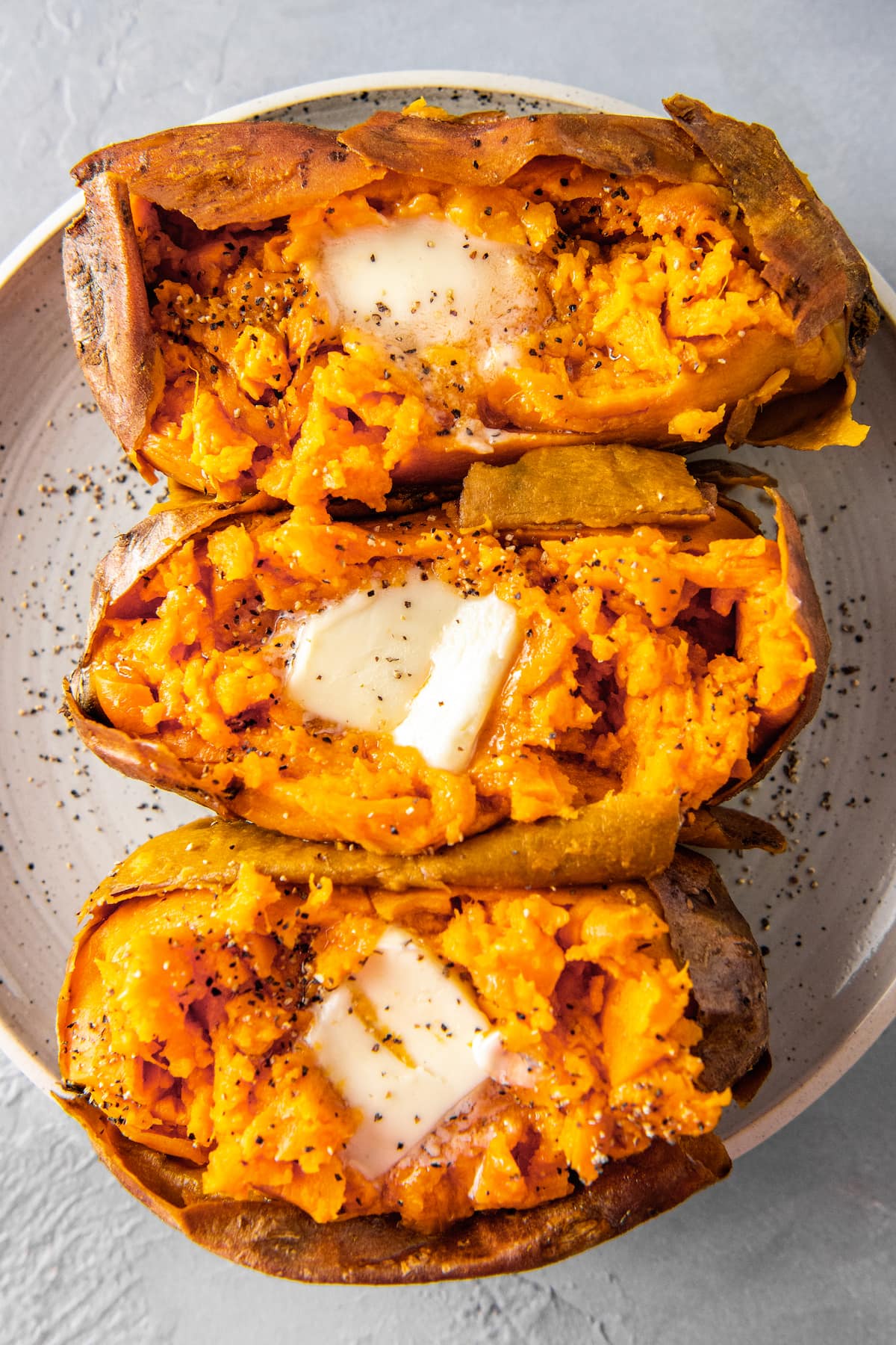 three baked sweet potatoes with butter, salt, and pepper on a plate