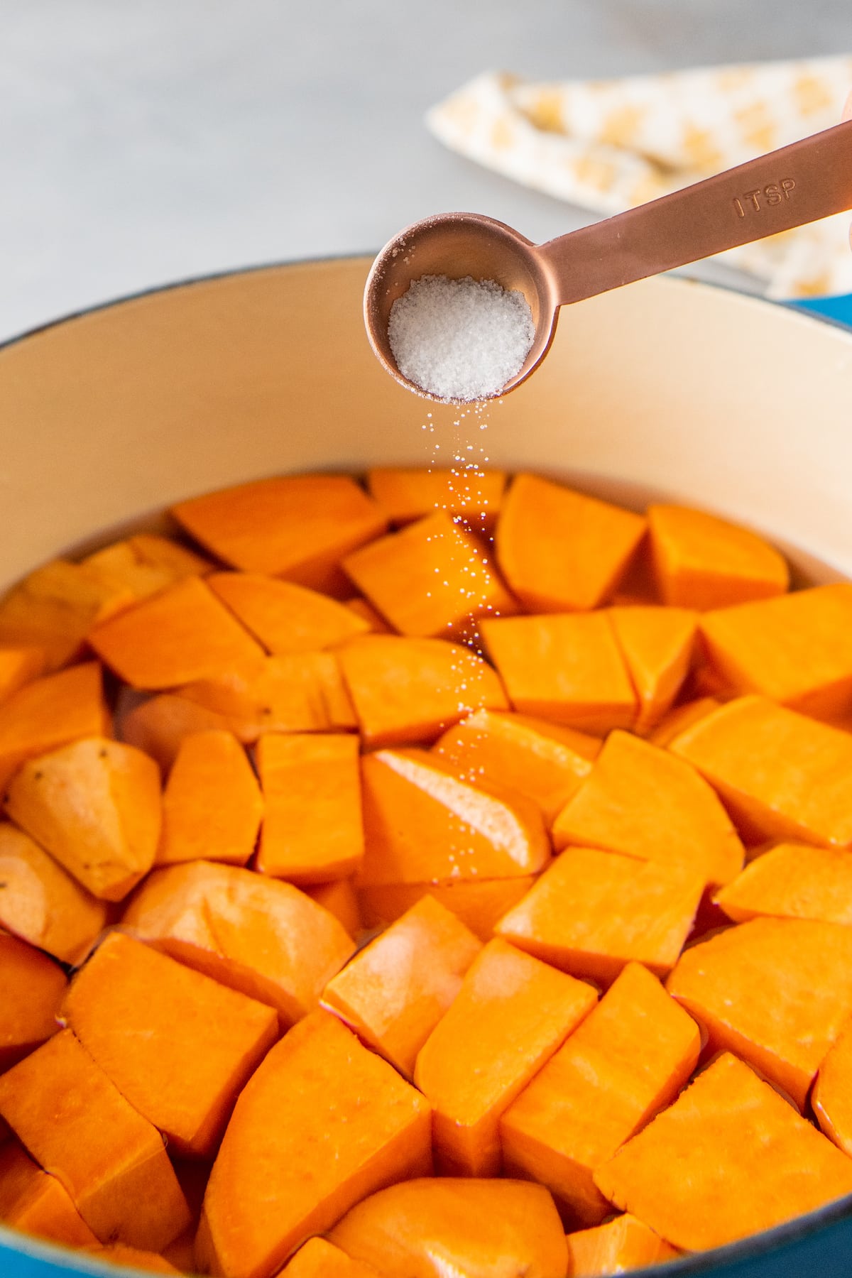 cubed sweet potatoes in water and being seasoned with salt