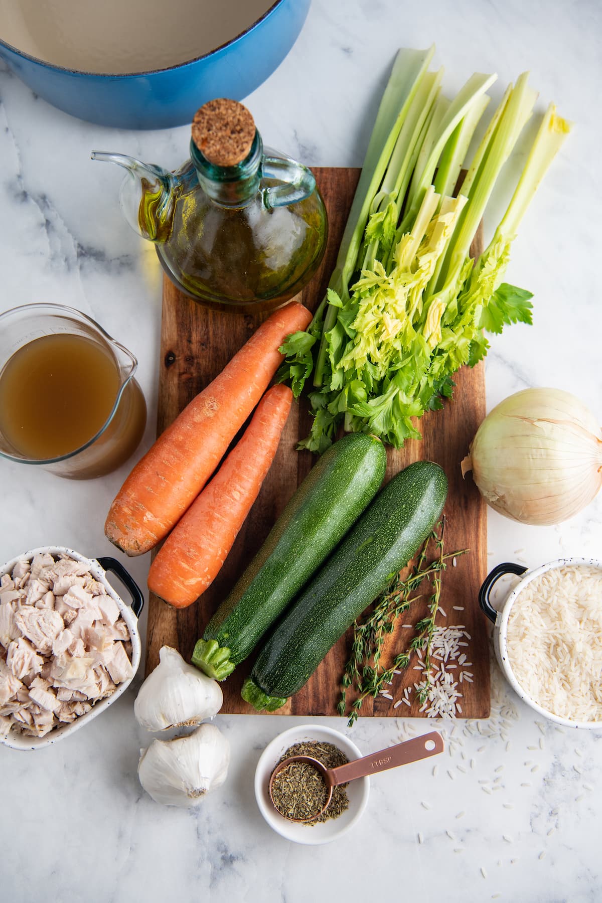 cutting board with an assortment of fresh vegetables alongside other ingredients like broth and chicken to make soup