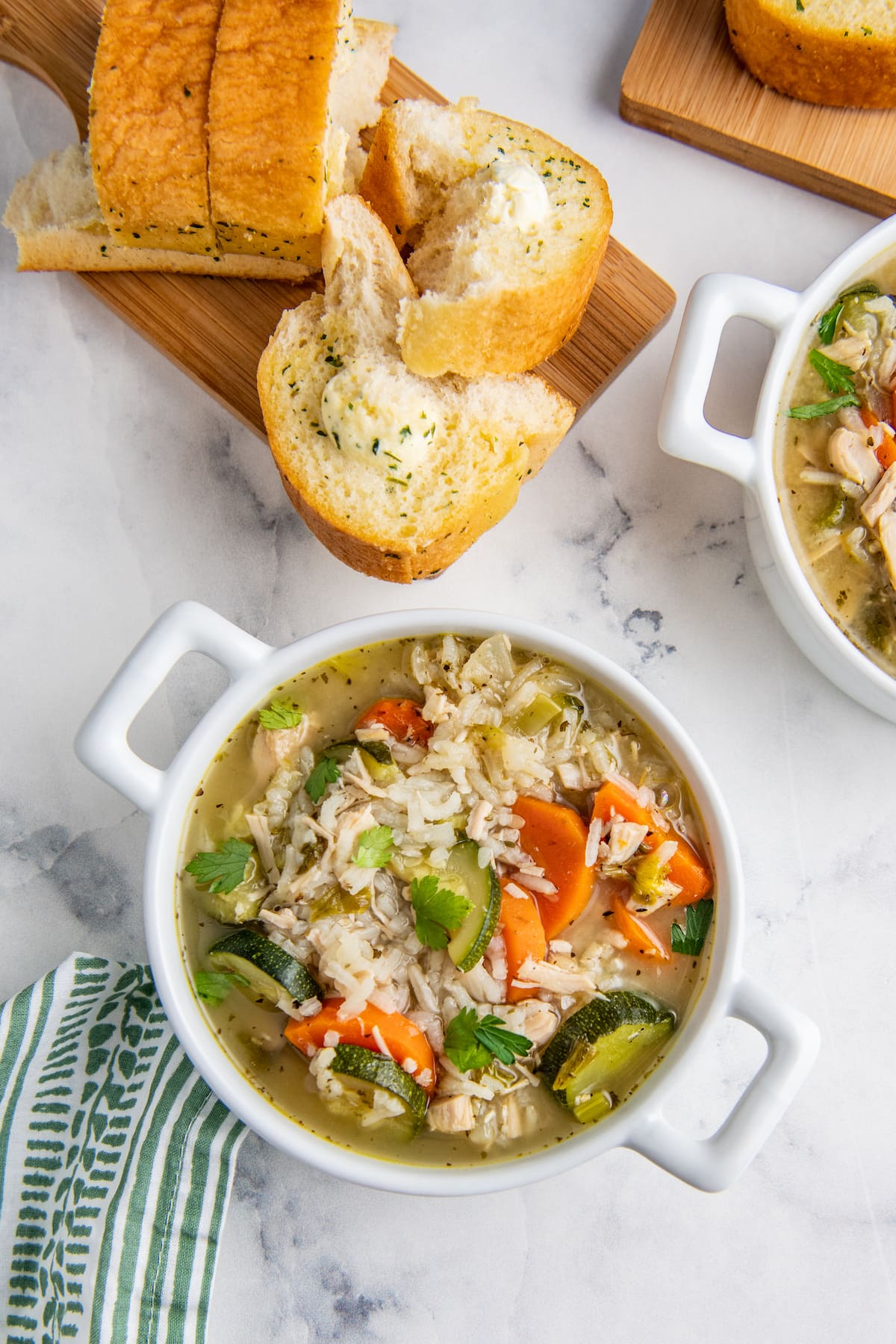 a soup bowl with chicken, rice, and vegetable soup alongside some pieces of bread