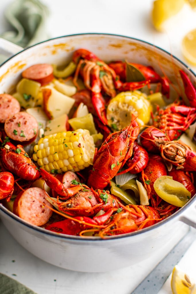 A crawfish boil in a white pot with herbs on top.