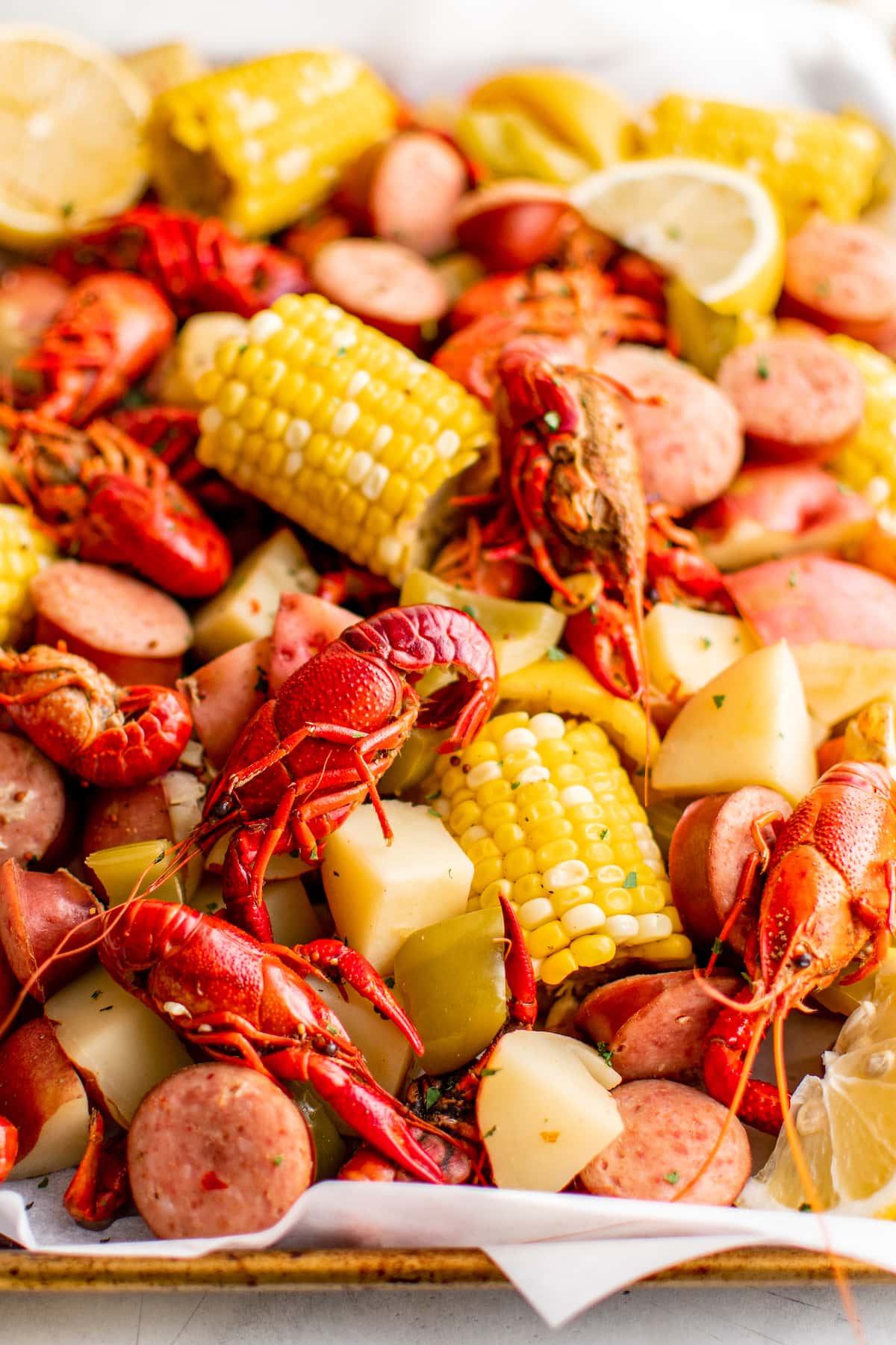 Crawfish, corn, potatoes, onion and more on a sheet pan lined with parchment paper.