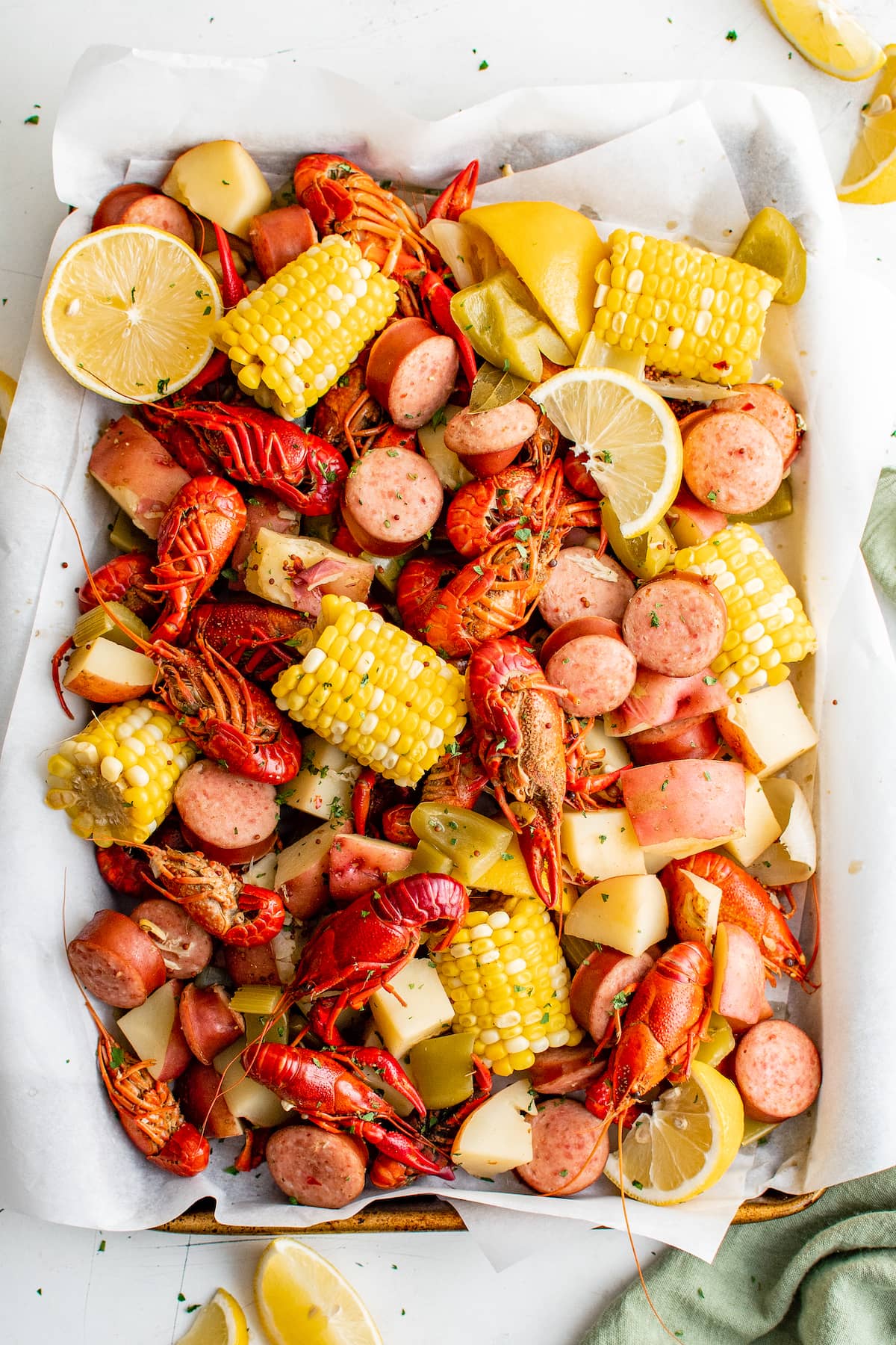 A sheet pan filled with boiled crawfish, corn, potatoes, and lemon wedges.