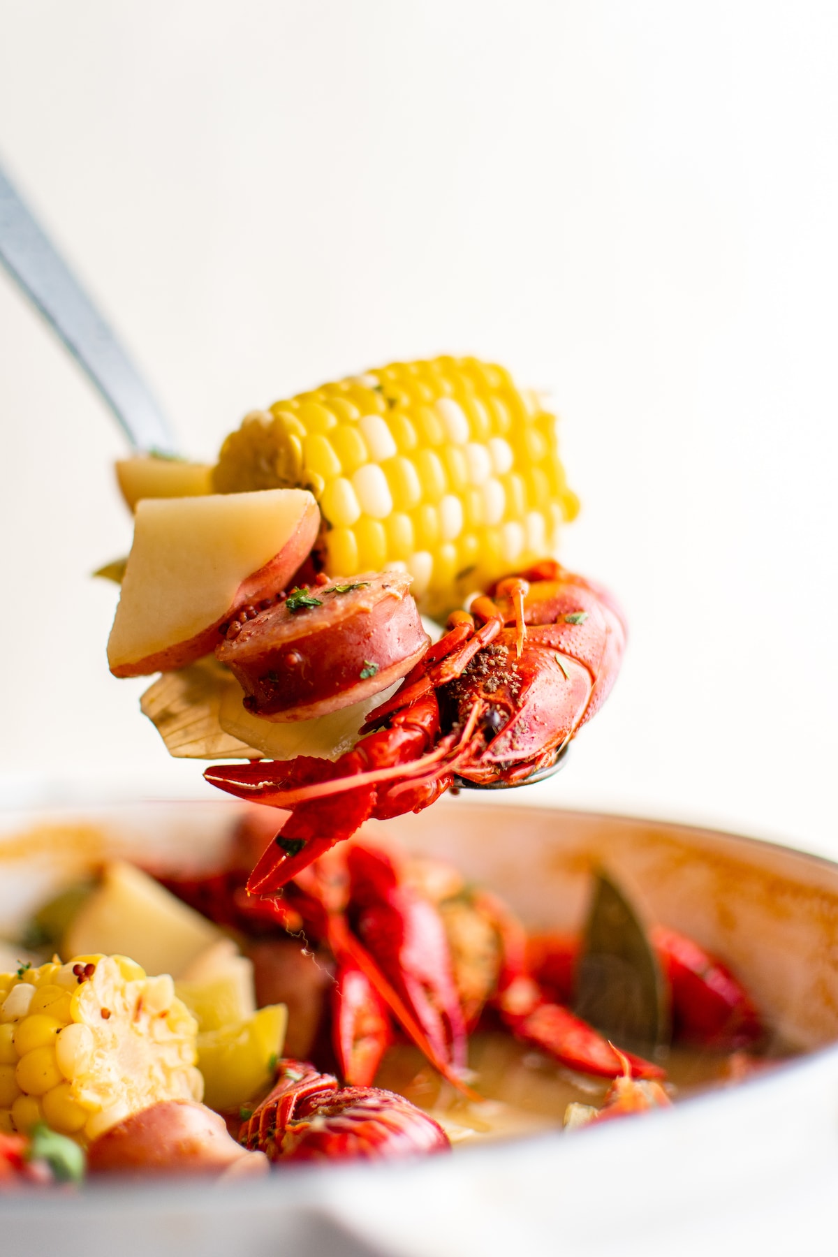 A ladle scooping up a serving of crawfish boil out of a large white pot.