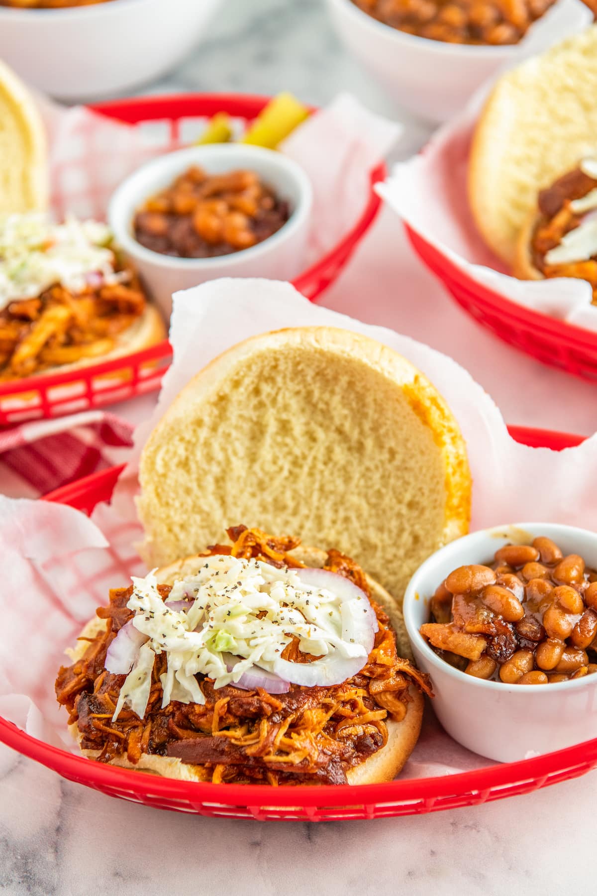 BBQ Chicken sandwiches with onions and slaw on top in baskets with baked beans.