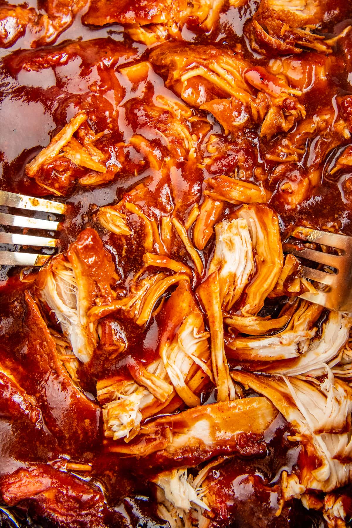 Chicken breasts shredded in bbq sauce with two forks inside a crockpot.