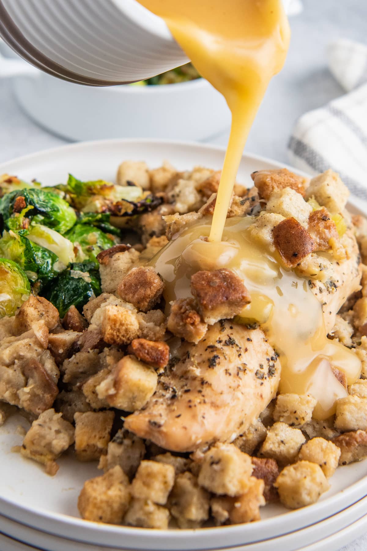 gravy being poured over a plate of cooked chicken with stuffing and a side of Brussels sprouts