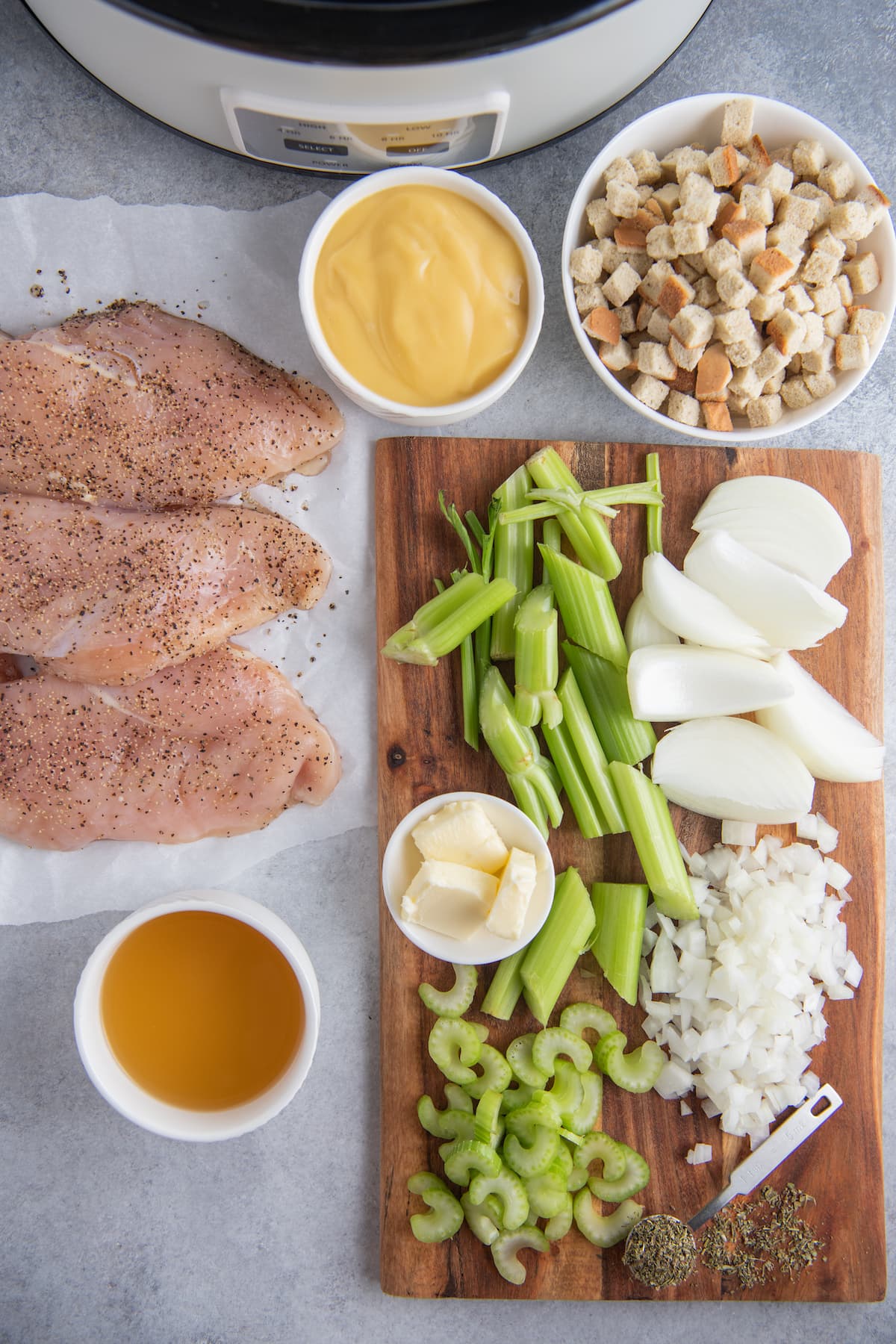 A display of ingredients prepped for a crockpot dinner - chicken, chopped vegetables, cream of chicken soup, bread pieces, and stock