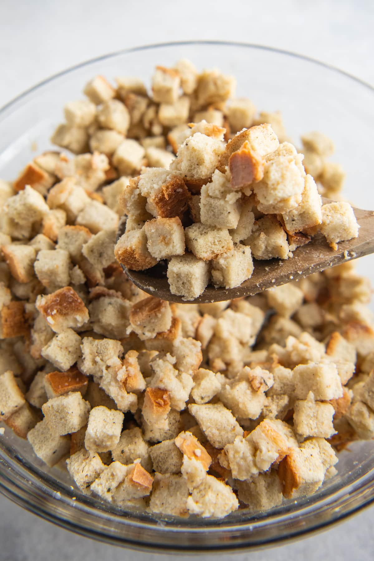 a bowl of cubed stuffing after being tossed with stock, a spoon showing a close up of a scoop