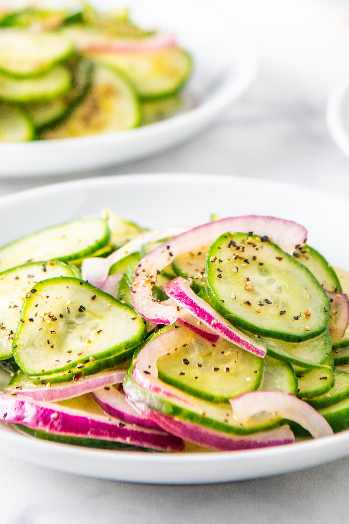 Sliced cucumbers and red onions tossed in a homemade vinaigrette on a white plate.