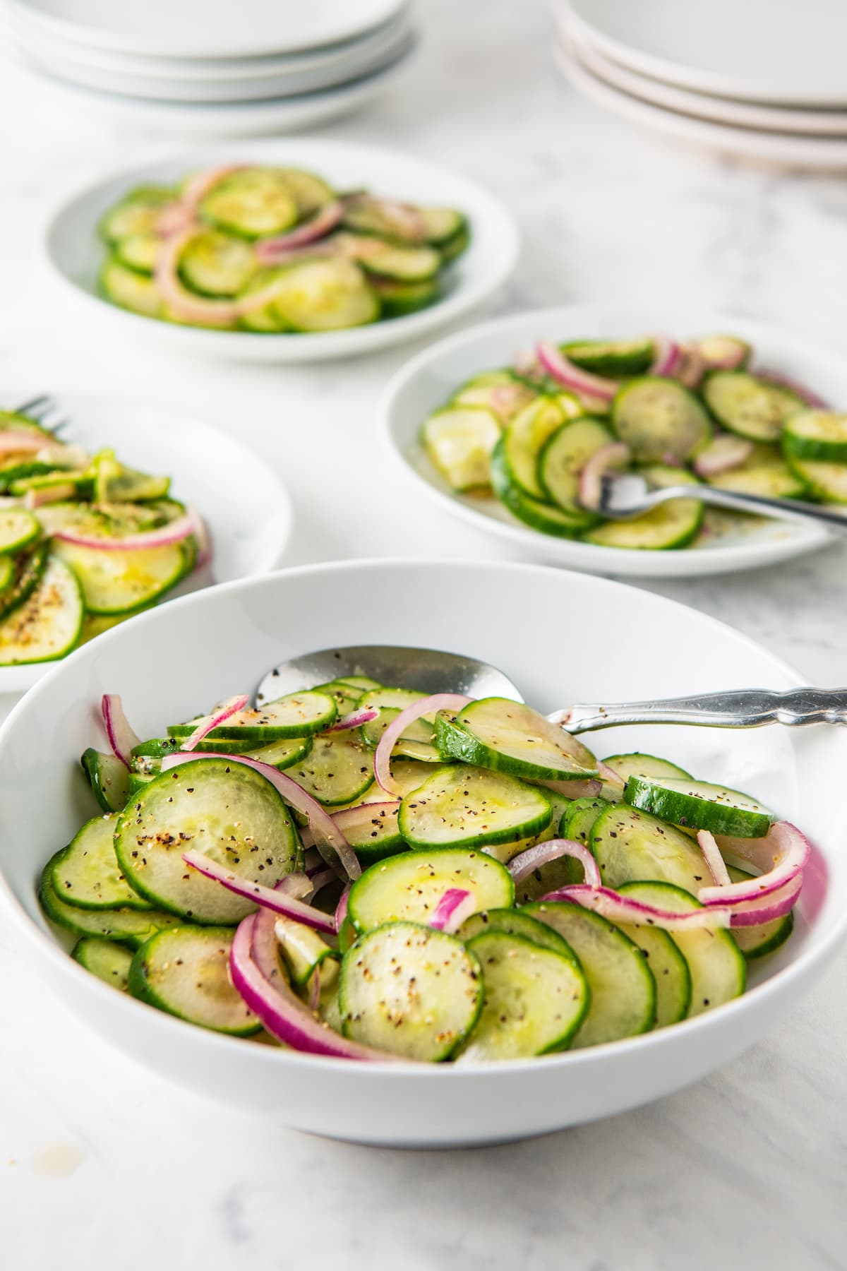 A bowl of healthy cucumbers and onion salad with many plates filled with salad behind the bowl.
