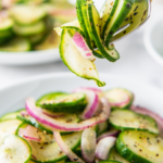 A fork picking up a bite of cucumber salad off a plate.