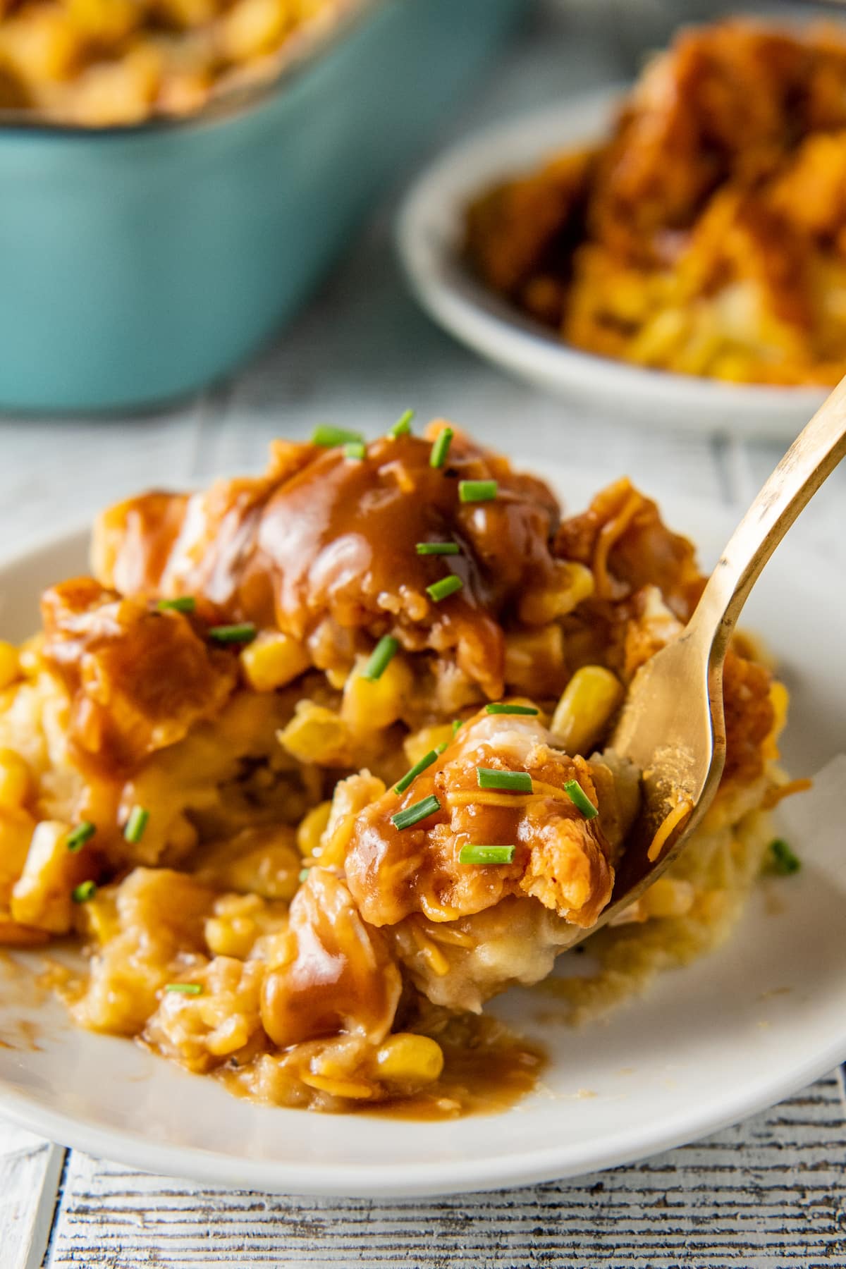 close up of a slice of fried chicken casserole with mashed potatoes, corn, cheese, and gravy on a serving plate