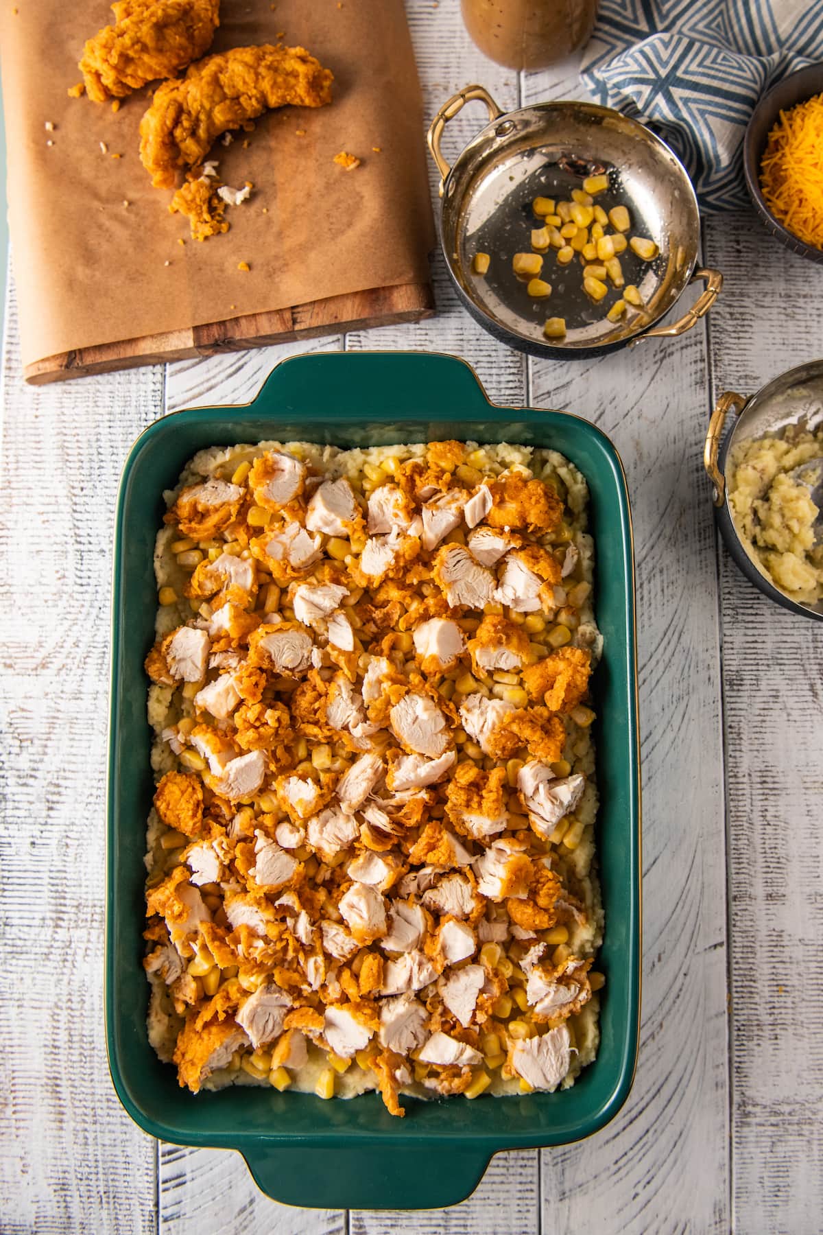 fried chicken spread evenly on top of mashed potatoes and corn in a casserole dish