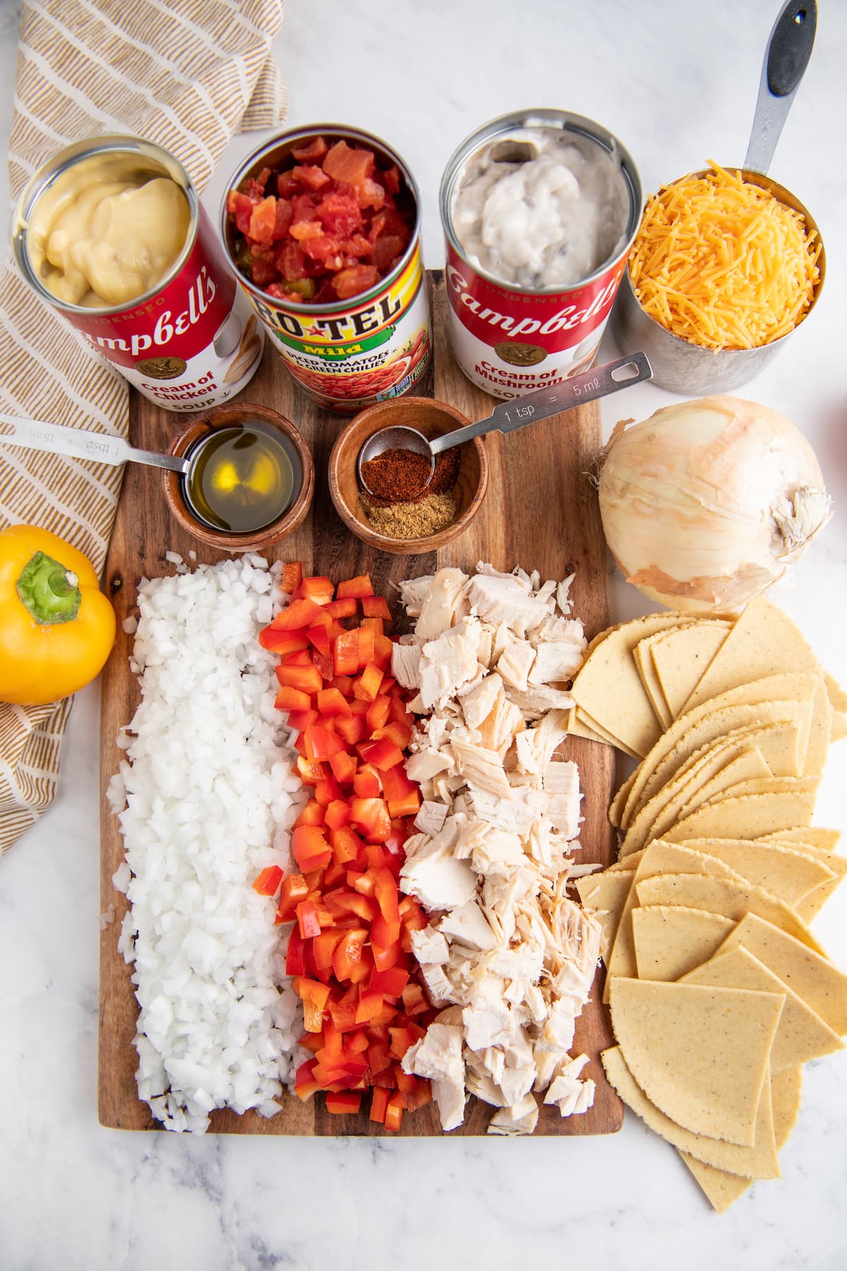 Ingredients to make a Mexican-inspired chicken casserole including tortillas, chicken, peppers, onions, canned chicken soup, tomatoes, seasonings, olive oil, and cheese