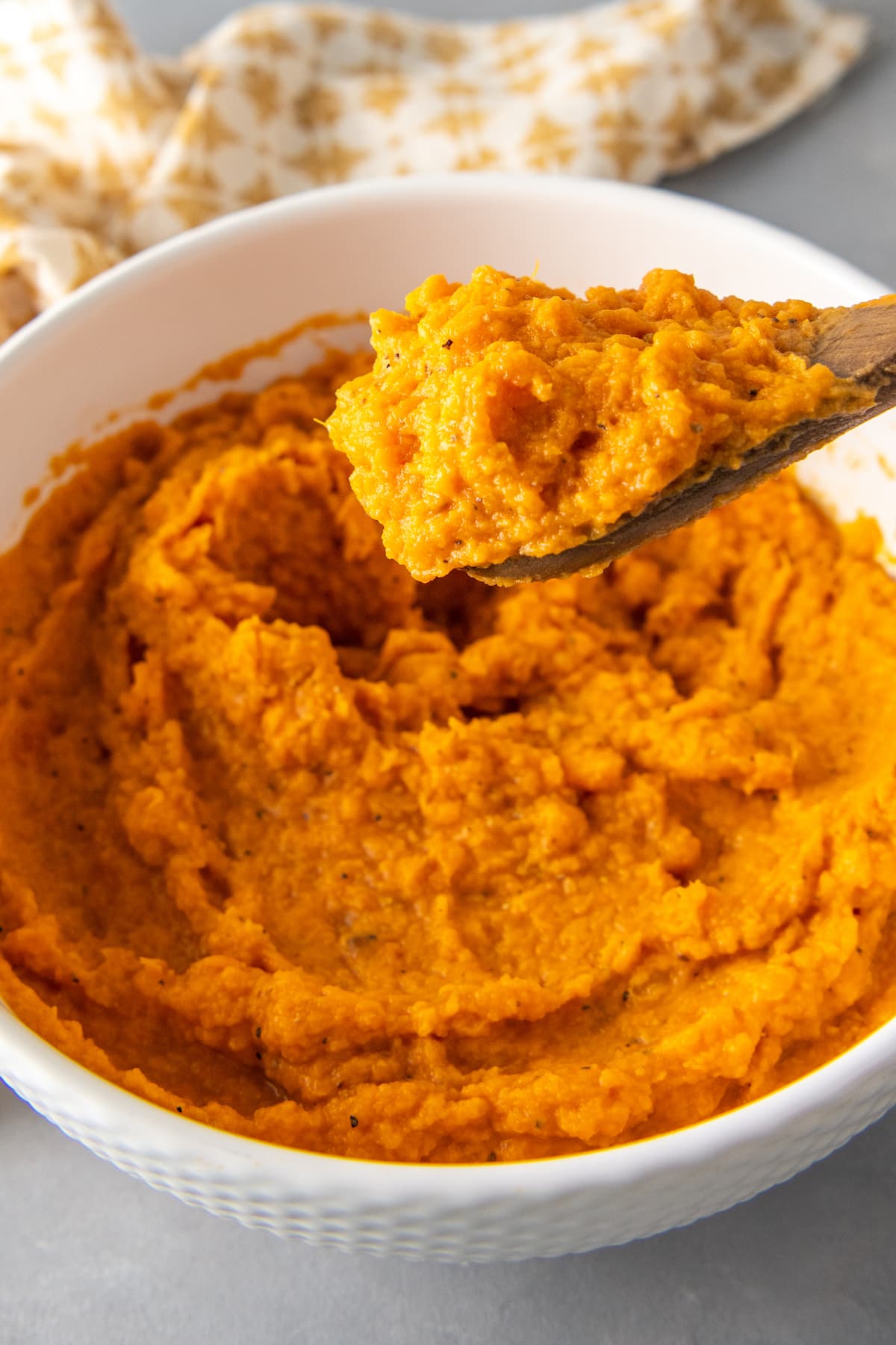 a bowl of mashed sweet potatoes with a wooden spoon taking out a portion