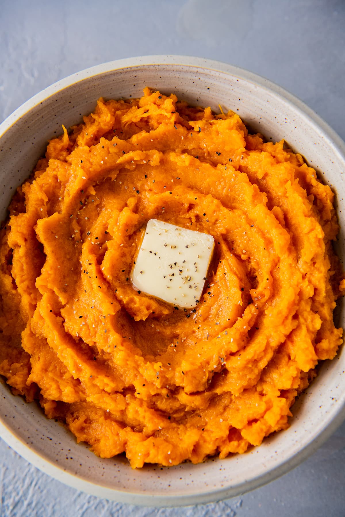 a bowl of mashed sweet potatoes with a pad of butter in the middle