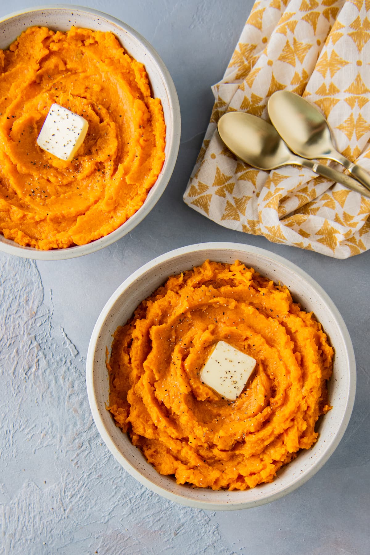 two bowls of mashed sweet potaotes next to a cloth napkin with spoons on it