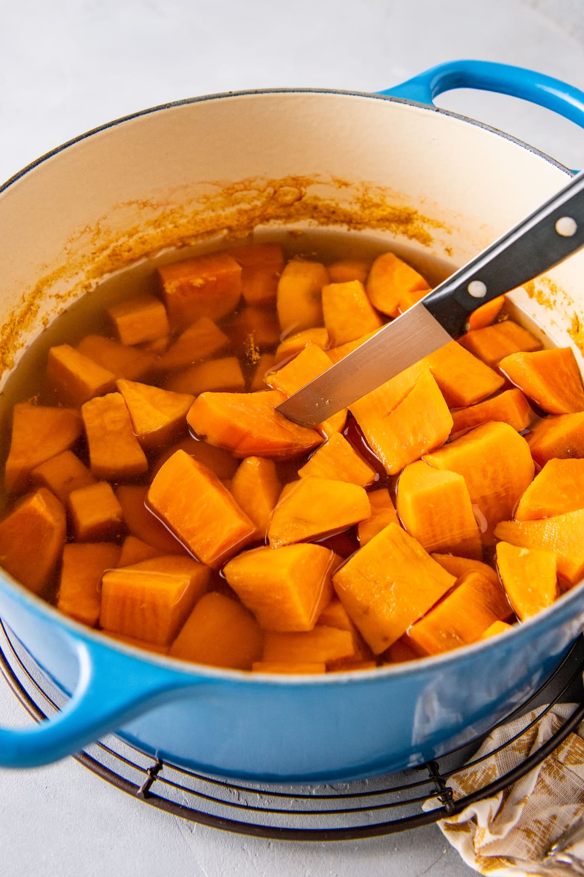 a knife checking doneness of cubed sweet potatoes in a pot