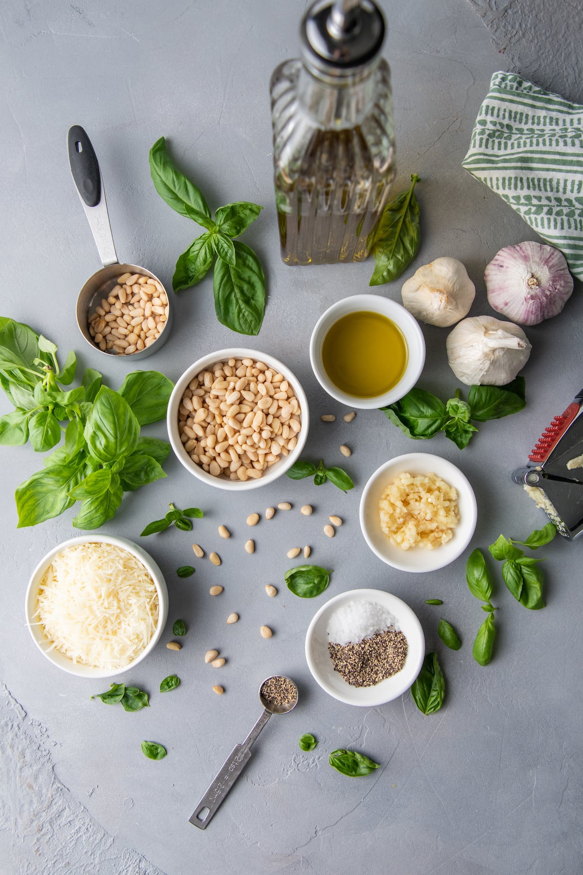 all of the ingredients you need to make fresh pesto like basil, garlic, parmesan cheese, salt, pepper, pinenuts, and olive oil in seperate prep dishes