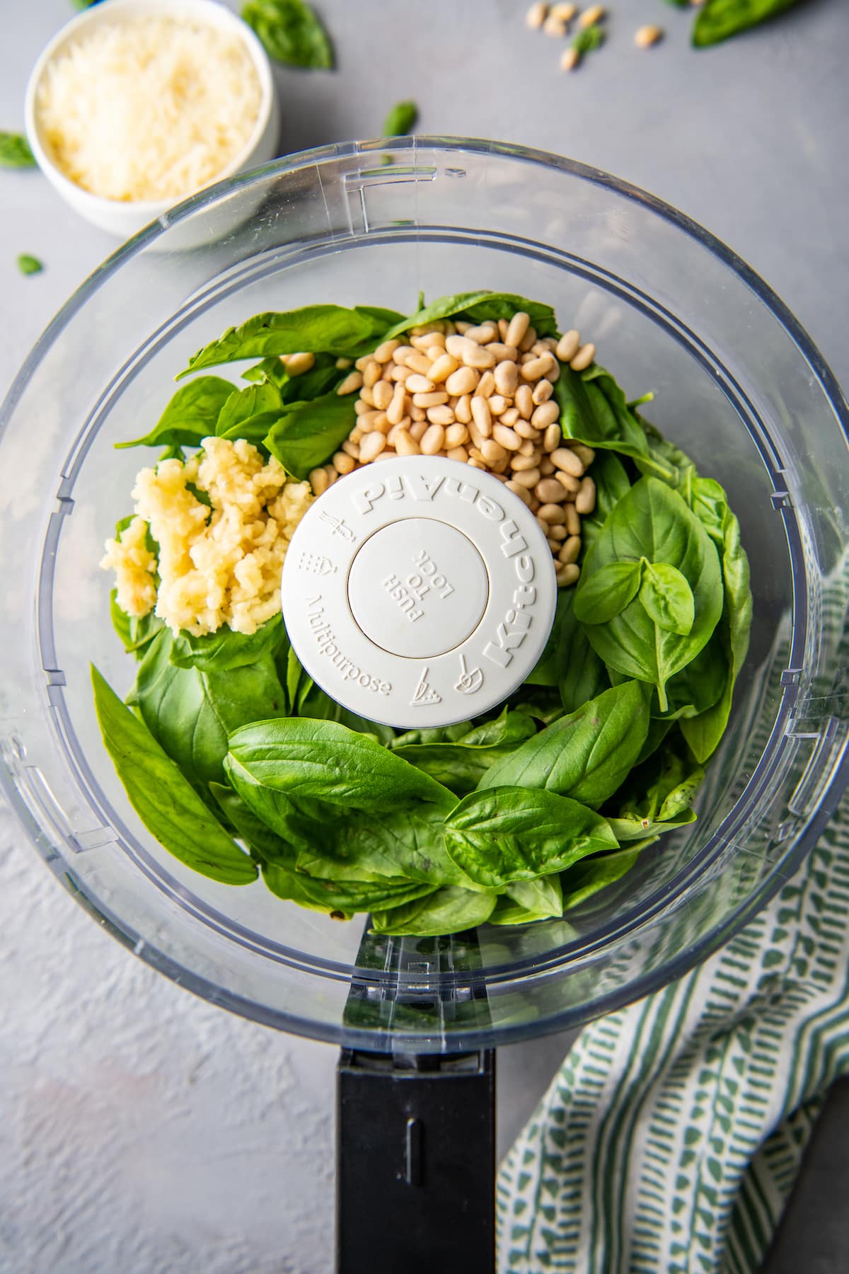 food processor with basil leaves, pine nuts, and garlic
