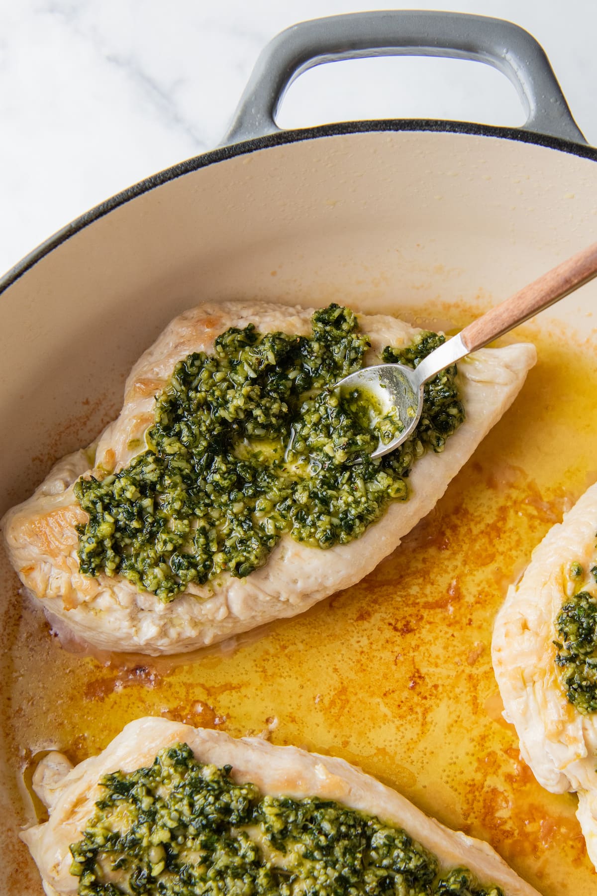 a cooked chicken breast with pesto being spread on top with a spoon