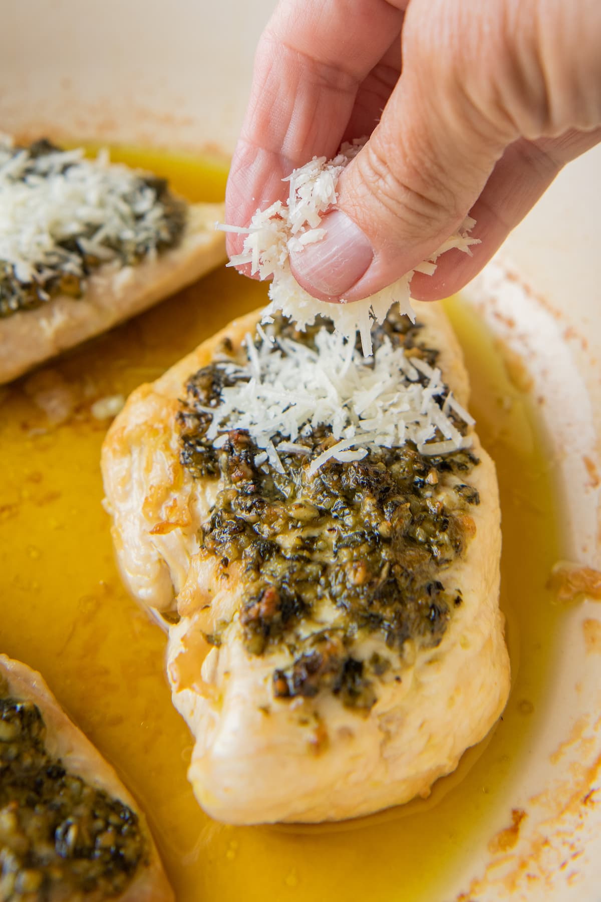 garnishing a cooked chicken breast with pesto with some shredded parmesan cheese