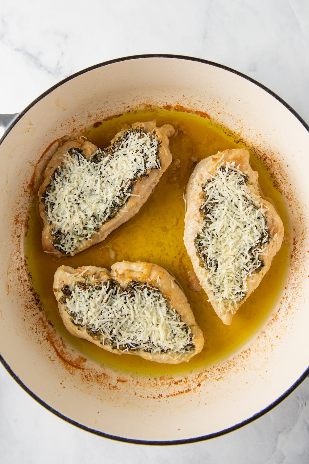 three chicken breasts garnished with basil pesto and parmesan cheese