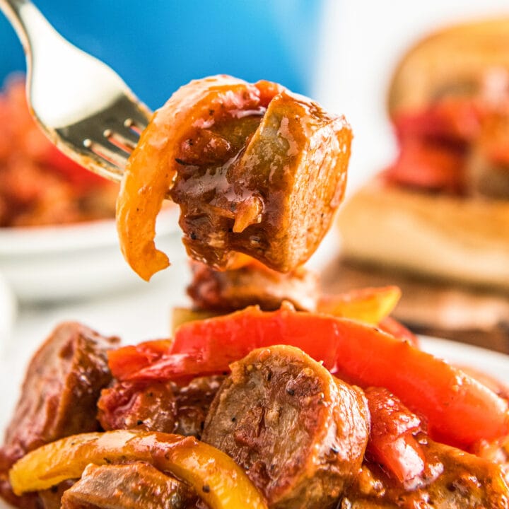 A fork picking up a bite of Sausage, Peppers, and Onions off a plate.