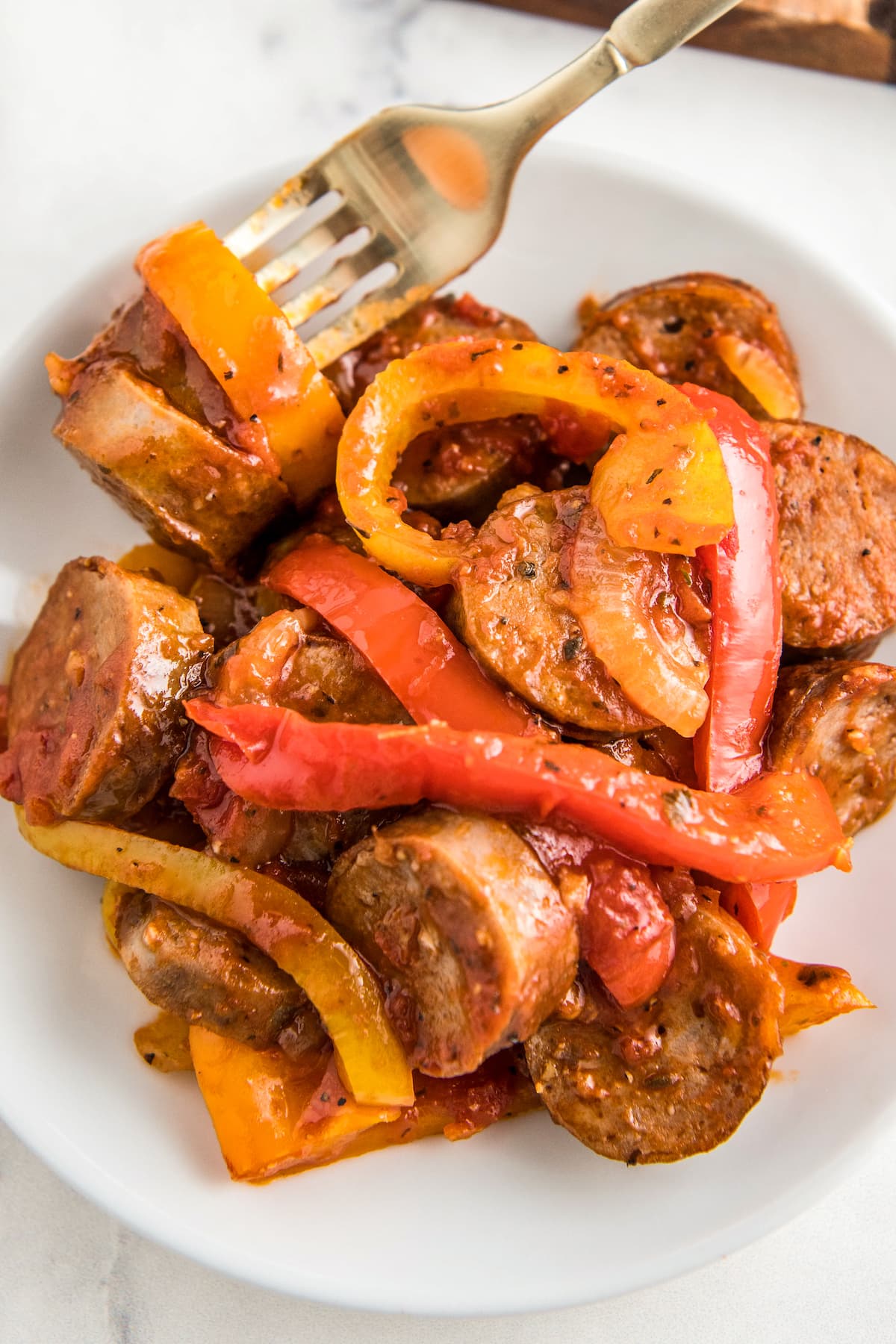 A plate with a fork filled with onions, peppers and sausage.
