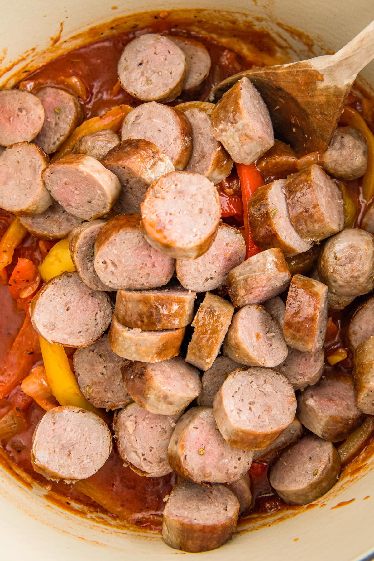 Sliced sausage being added to a pot with onions and peppers in the bottom.