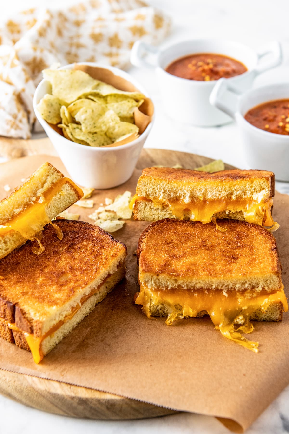 two grilled cheese sandwiches cut in half on a wooden platter with a side of potato chips
