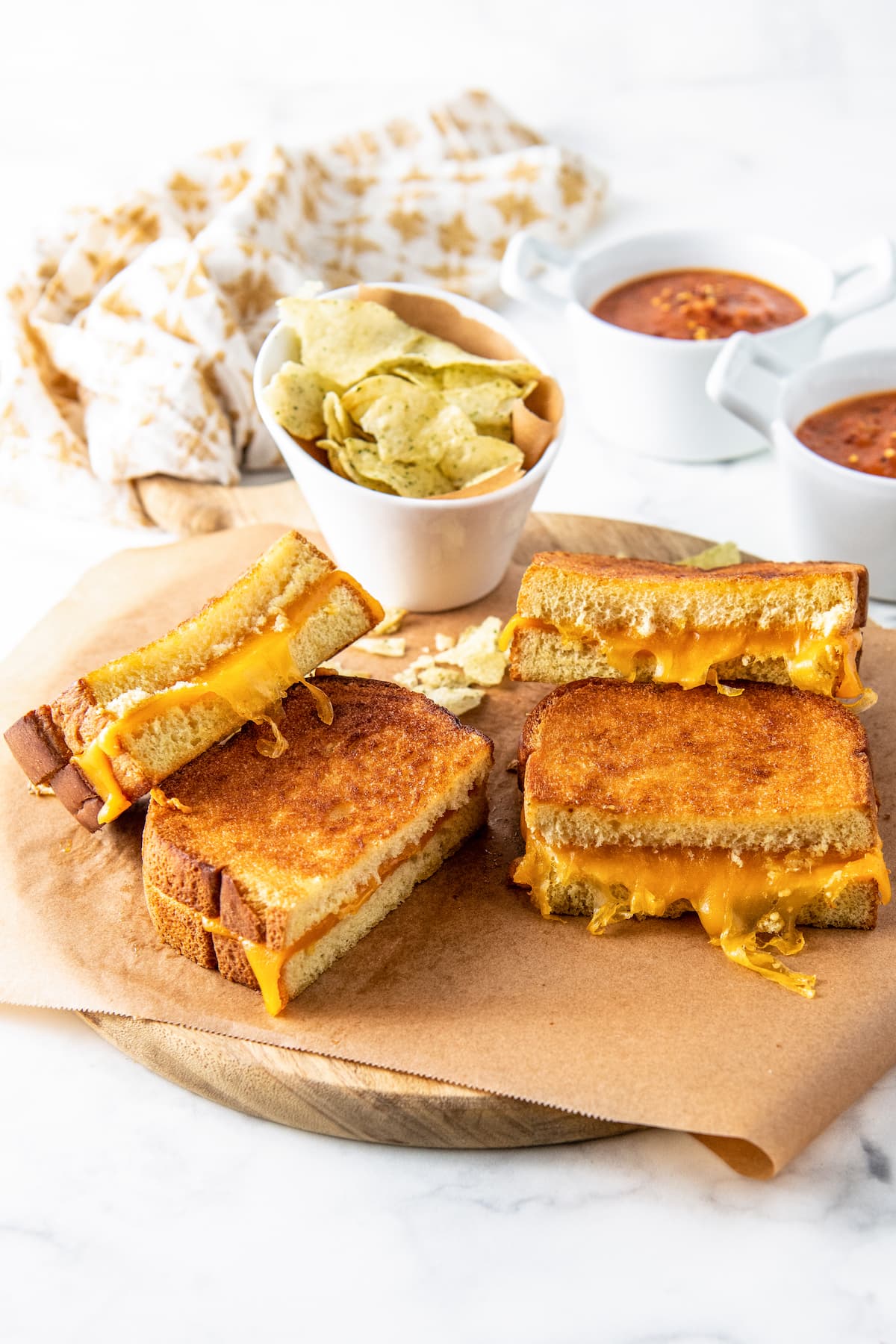 two grilled cheese sandwiches cut in half on a wooden platter with a side of potato chips